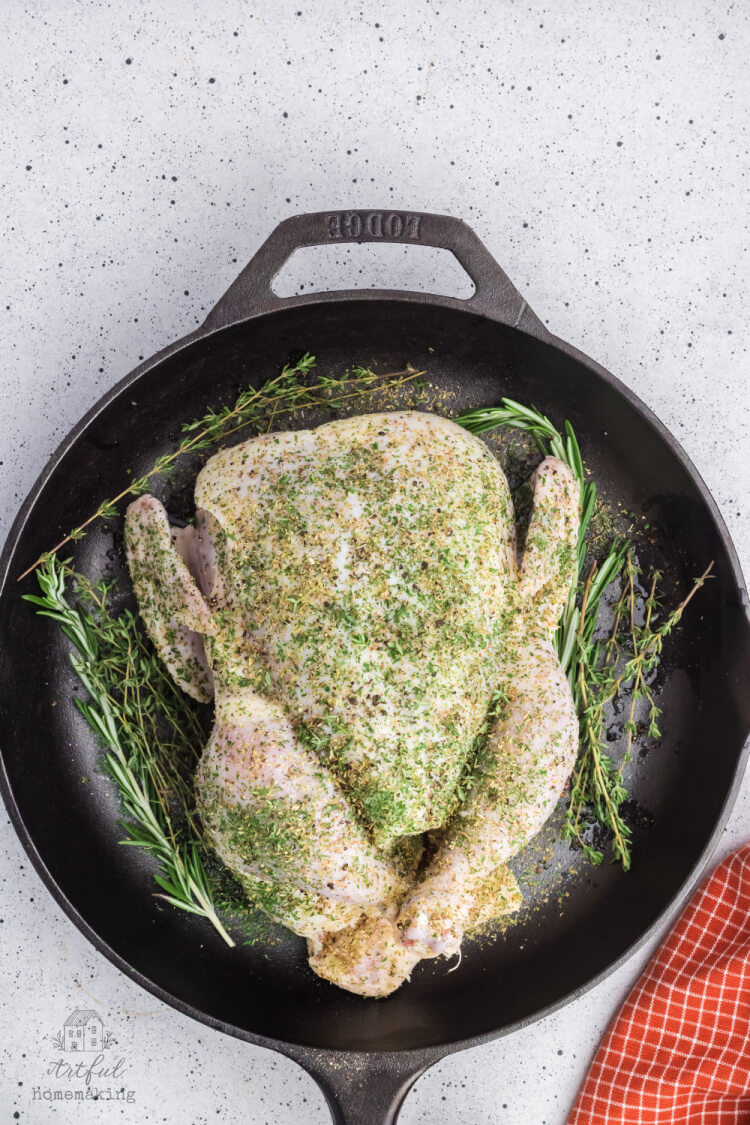 raw chicken with herbs sprinkled on it in a cast iron skillet